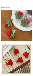 Detailed view of 3D strawberry hair clips set on a velvet display and wooden table
