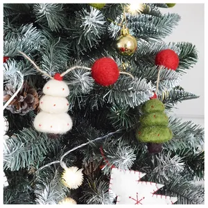 Detail von Weihnachtsbaumanhängern aus Wollfilz mit roten Kugeln an einem Kiefernzweig