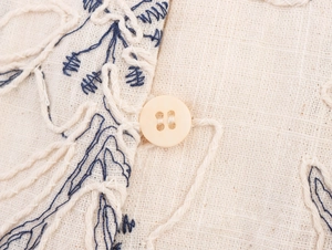 Macro detail of beige cotton linen fabric with floral embroidery and button detail