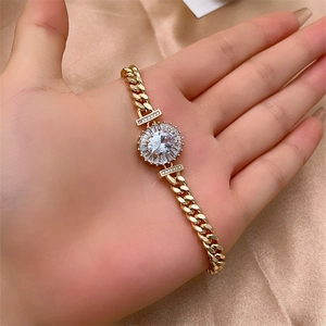 Close-up of golden curb chain bracelet with oval zircon centerpiece on satin