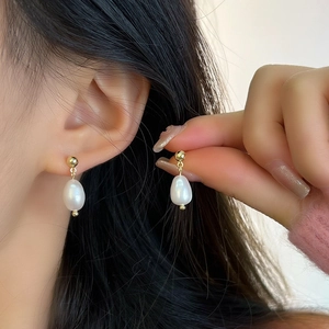 Close-up of elegant baroque freshwater pearl drop earrings with golden studs on a model