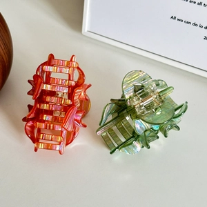 Floral acetate hair claws in iridescent orange and green on a white surface