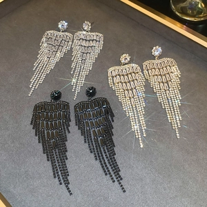 Close-up of sparkling floral tassel earrings in silver, gold, and black on a grey tray