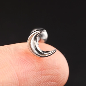 Close-up of a tiny silver crescent moon zircon stud earring held on a fingertip