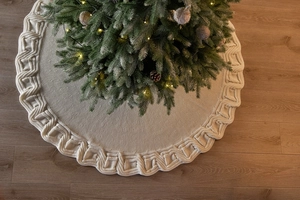 Detail of cream-white knitted Christmas tree skirt with textured wave patterns on wood floor