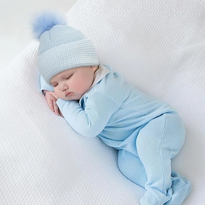 Light blue knit baby romper set with matching pom-pom hat on a white waffle blanket