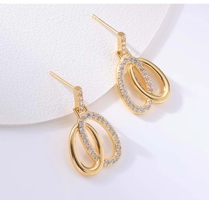 Close-up of gold double oval earrings with pavé zircons on white leather background
