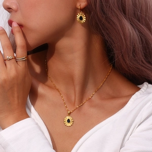 Detail of a model wearing a gold water wave chain necklace with a black flower pendant