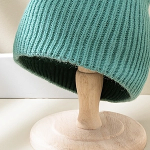 Minimalist lake green ribbed knit beanie hat for winter on a wooden stand
