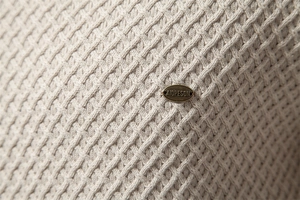 Detail of light beige cotton knit sweater showing texture and bronze oval metal logo