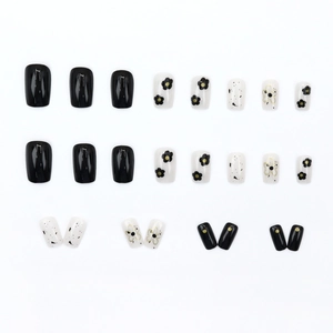 Short square press-on nails with black and white flower patterns and gold trim accents