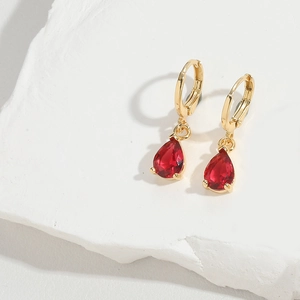 Detailed view of red pear-shaped gemstone earrings on a white stone background
