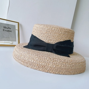 Close-up of a natural raffia boater hat featuring a wide black grosgrain ribbon bow