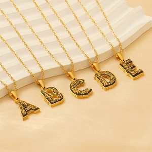 Detail of five gold chain necklaces featuring black textured letter pendants A to E