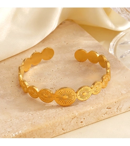 Golden stainless steel cuff bracelet with sunburst pattern on beige stone texture
