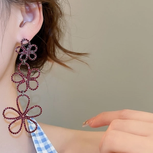 Detail view of long dangling floral earrings with red rhinestones on a female model