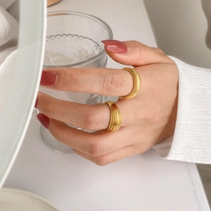 Detailed view of gold multi-layer ring and textured spring band on hand with water glass