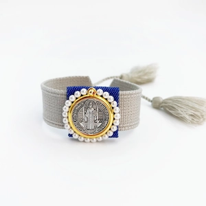 Detail of St. Benedict medal on woven bracelet with white pearls and tassel accents