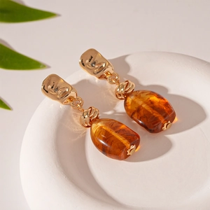 Detail of amber acrylic and gold metal geometric earrings on a white plaster tray