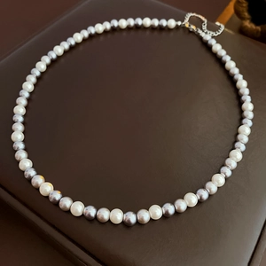 Detail of elegant two-tone white and grey pearl necklace with silver lobster clasp