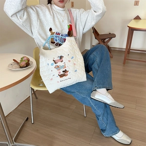Detail of white quilted crossbody bag featuring cute cartoon dog embroidery in a cafe setting