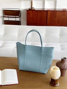 Blue hand-woven PVC straw tote bag for summer beach vacation on a wooden coffee table