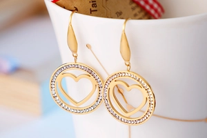 Detail of gold heart earrings with zircons hanging on a white porcelain cup as a gift