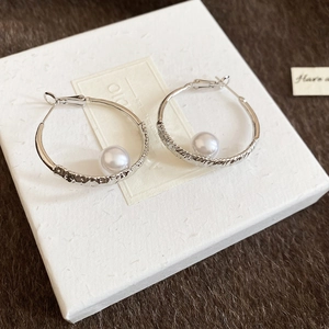Detail of silver pearl hoop earrings with irregular hammered texture on white paper box
