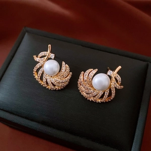 Macro detail of 18k gold plated feather earrings with white pearl and micro-inlaid zircons