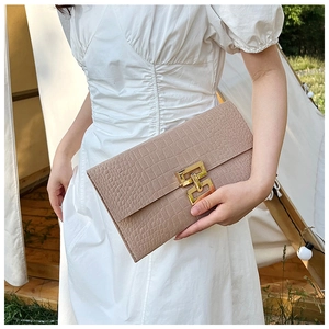 Close-up of beige crocodile pattern felt clutch with gold H-shaped buckle detail