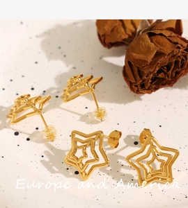 Macro detail of gold star stud earrings with hollow texture on a white tray