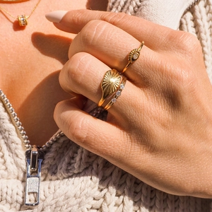 Macro view of 18k gold rings including sunburst signet and evil eye detail on hands