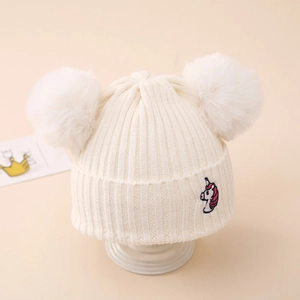 Close-up of winter knitted hat with double faux fur pom-poms and unicorn embroidery