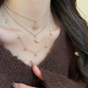 Close-up of triple-layered gold star and moon pendant necklace on a brown sweater