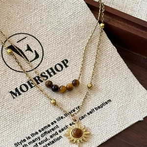 Macro shot of double-layered gold necklace with tiger eye beads and sunburst pendant