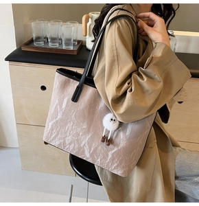 Ampia borsa tote beige testurizzata con ciondolo a pompon in un contesto di stile