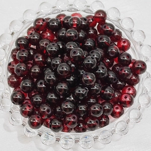 Macro shot of 4-8mm deep red glass beads in a glass bowl for DIY jewelry making