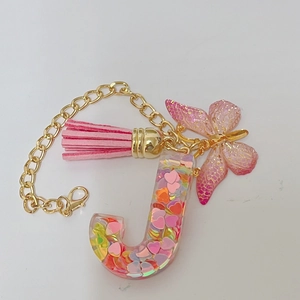 Detail of letter J keychain with pink tassel, butterfly charm and colorful heart sequins