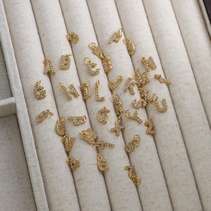 Gold letter charms with cubic zirconia on a beige velvet tray for DIY jewelry