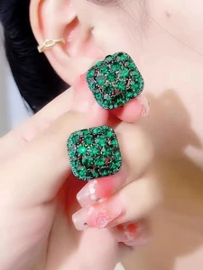 Close-up of model wearing emerald green geometric diamond earrings with gold ear cuff