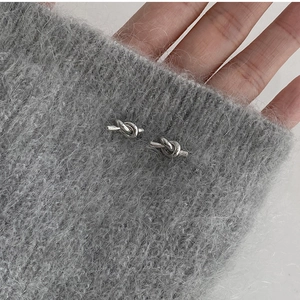 Macro shot of silver minimalist knot earrings on textured grey fabric background