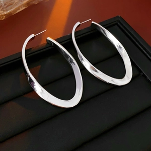 Close-up of oversized silver irregular oval hoop earrings on a black textured jewelry box
