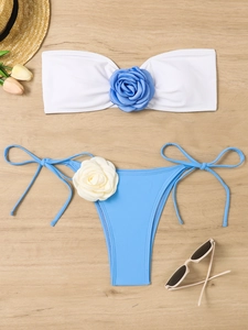 Flat lay detail of white bandeau bikini with 3D blue roses on a wooden beach background
