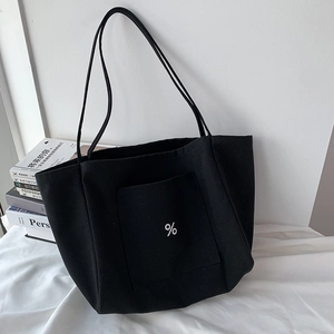 Close-up of black canvas tote bag with white percent sign pocket next to books