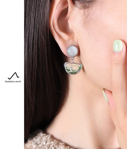 Close-up of stainless steel earrings with white cat eye and green resin stones on model