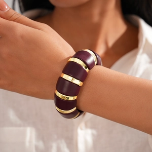 Close-up of chunky dark purple acrylic bracelet with golden spacers on a model wrist