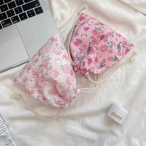 Flat lay of pink floral drawstring storage bags made of crinkled cotton on a white bed