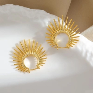 Macro shot of gold sunbeam earrings on a white ceramic plate with soft light