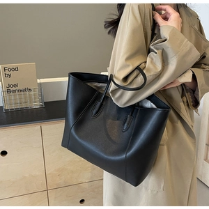 Detail view of a large black PU leather tote bag styled with a beige trench coat