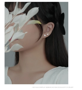 Close-up of polished silver butterfly stud earrings with sparkling zircon stones on a model